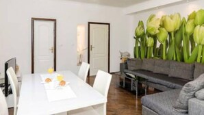 Uma sala de estar moderna com uma mesa de jantar branca, sofá cinzento e uma grande parede de tulipas verdes.