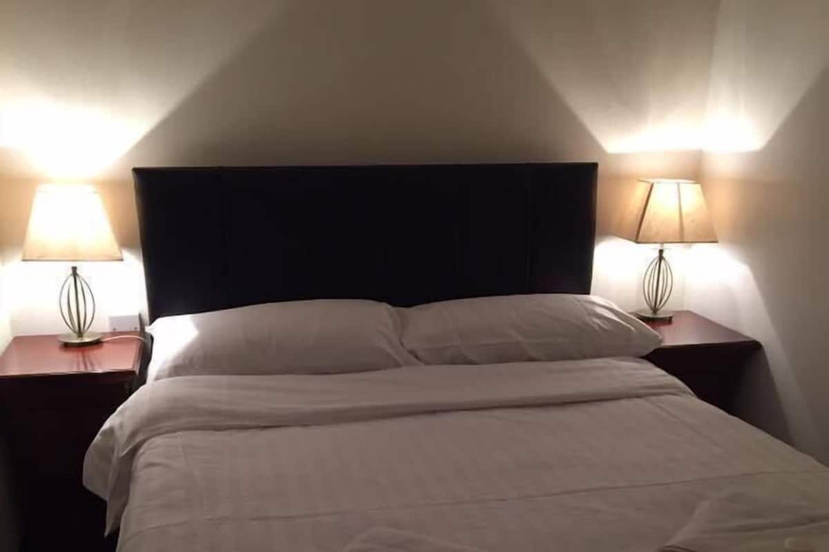 Ein Hotelzimmer mit einem großen Bett, zwei Nachttischen mit Lampen und einem dunklen Kopfteil.
