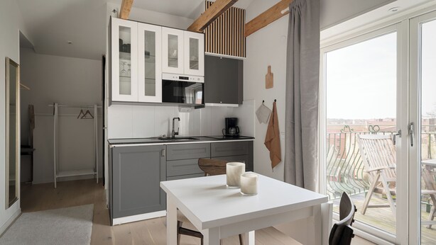 A modern kitchen with a dining area, a balcony with outdoor furniture, and a view of the city. - L Boutique Hotel (Lysekil)