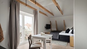 A modern room with a white table, a sofa, a TV, and a balcony with curtains. - L Boutique Hotel (Lysekil)