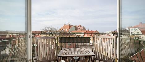 A balcony with a wooden table and chairs, a view of buildings in the background, and a clear sky.