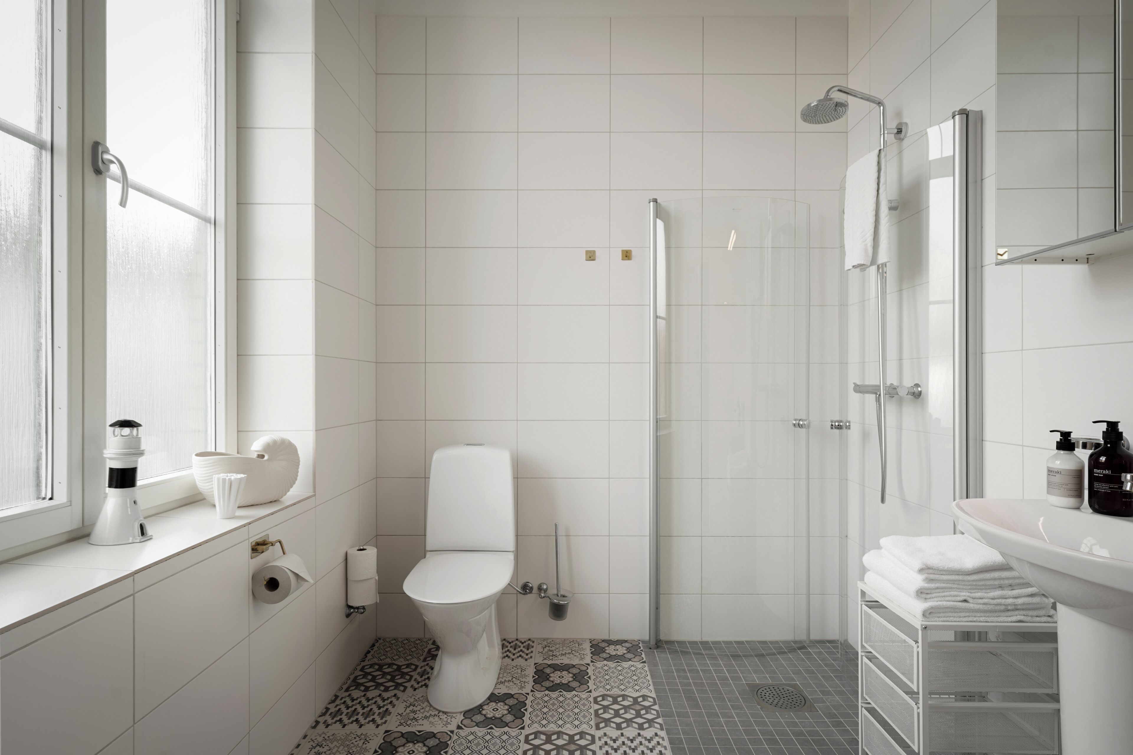 A modern bathroom with a toilet, shower, sink, and a window.