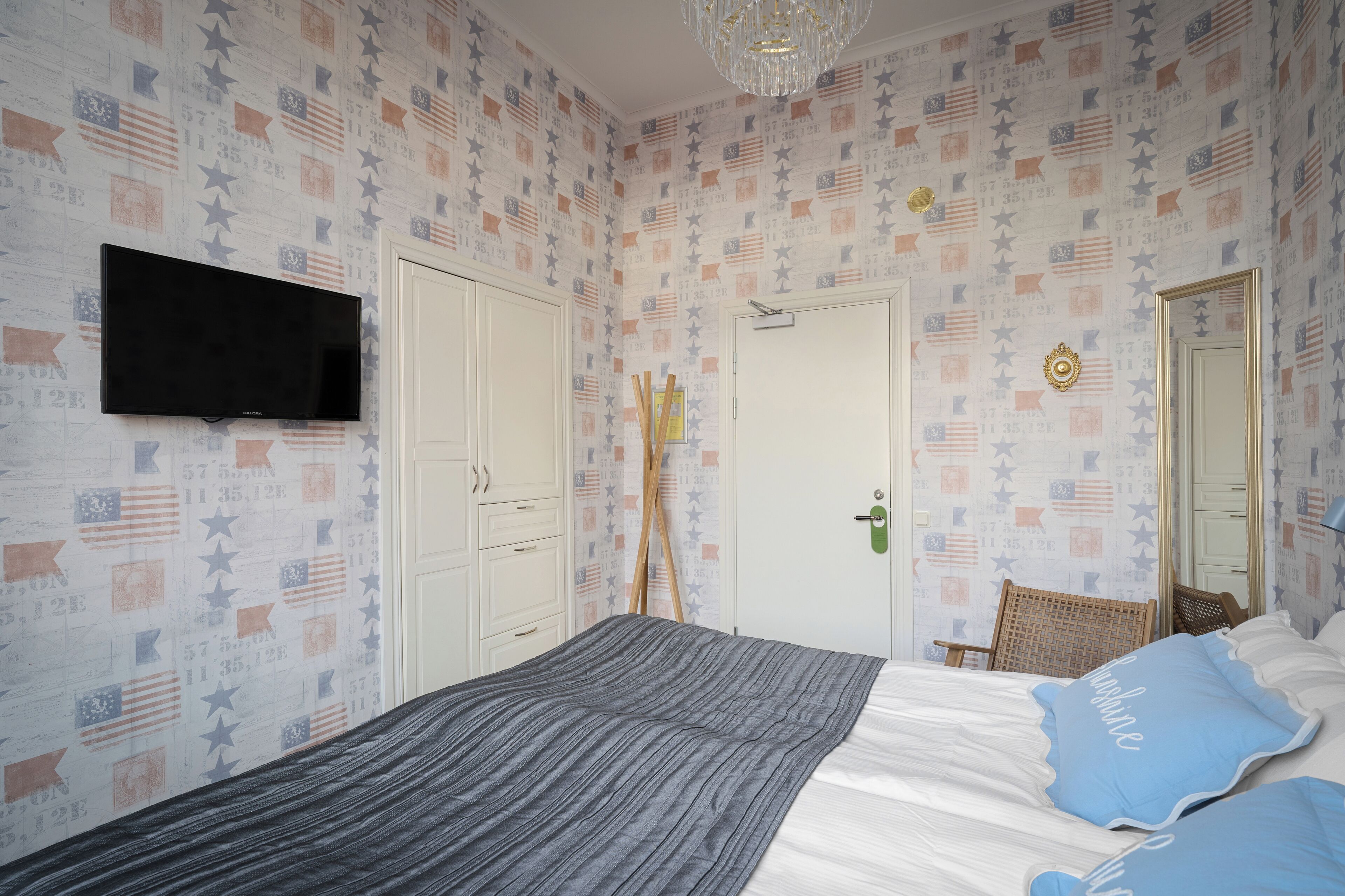 A bedroom with a bed, a television mounted on the wall, a door, and patterned wallpaper.