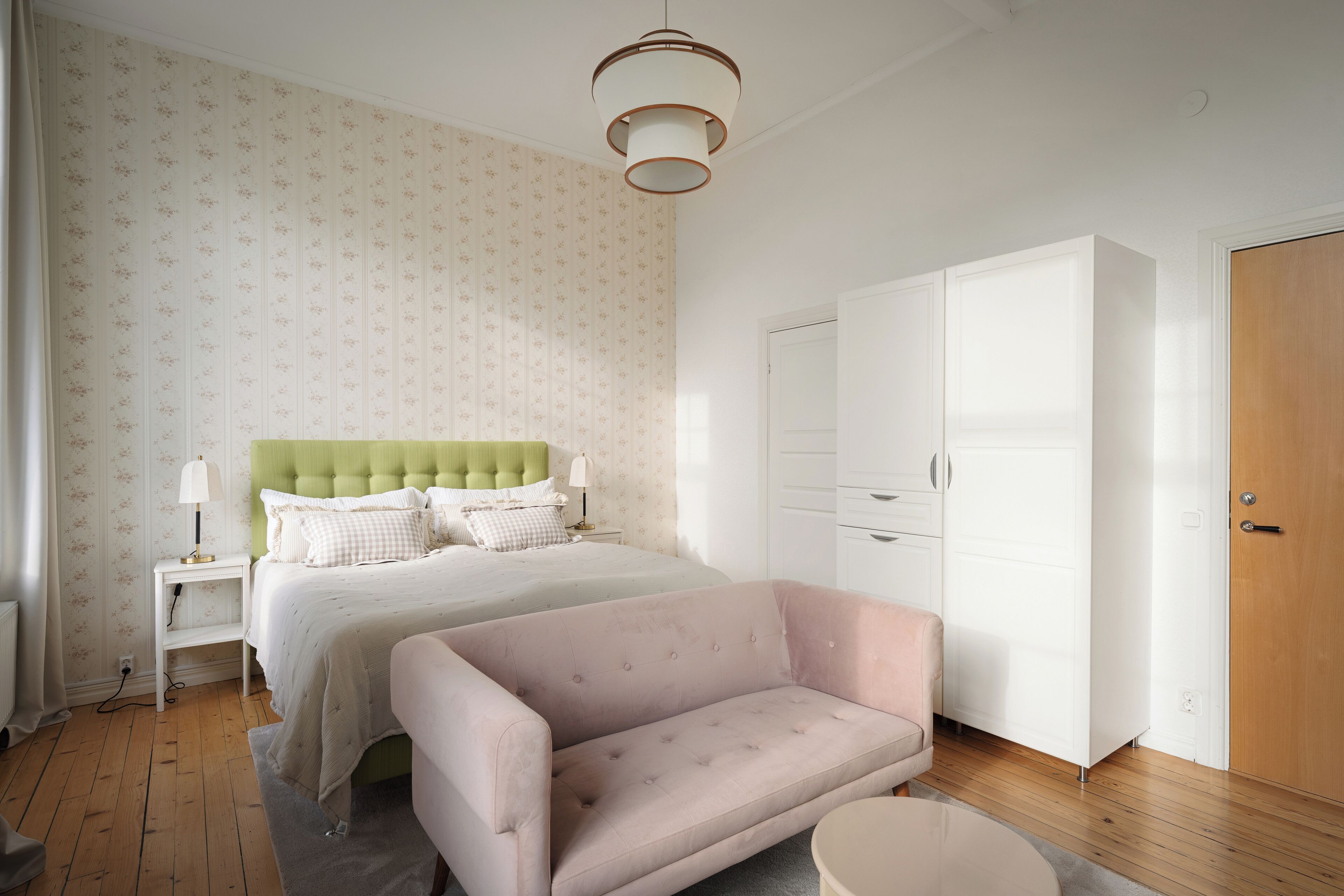 A bedroom with a bed, a green headboard, a white wardrobe, and a pink sofa.
