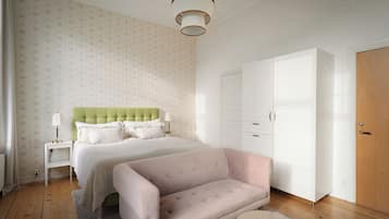 A bedroom with a bed, a green headboard, a white wardrobe, and a pink sofa.