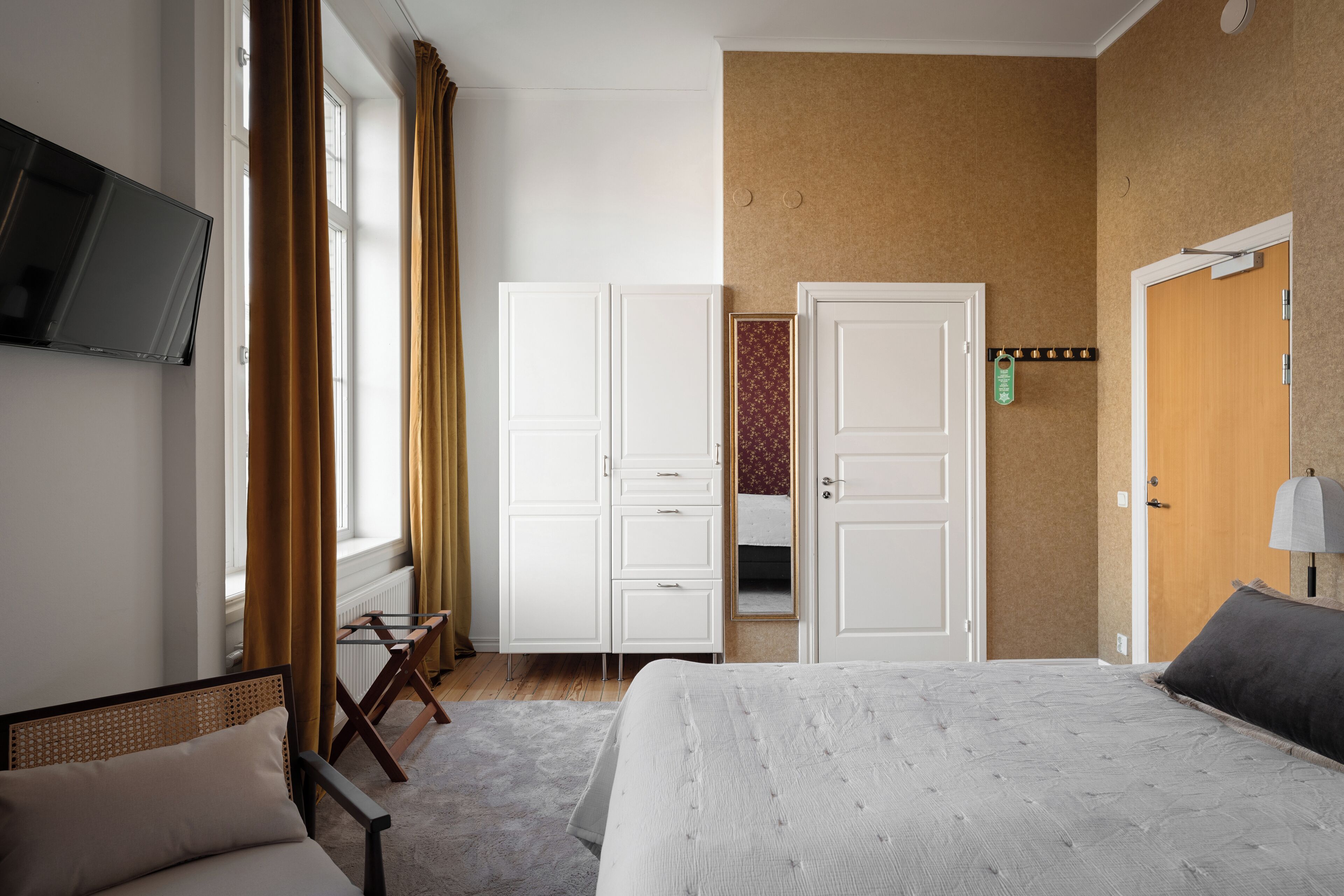 A hotel room with a bed, a chair, a wardrobe, a television, and a door.