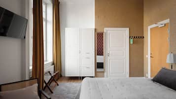 A hotel room with a bed, a chair, a wardrobe, a television, and a door.
