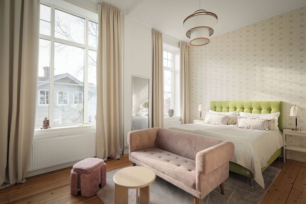 A bedroom with a green upholstered bed, a pink armchair, a round table, and a large window with curtains. - L Boutique Hotel (Lysekil)