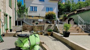 A vintage green scooter parked on a paved street with a stone wall and steps leading to a building. - L Boutique Hotel (Lysekil)