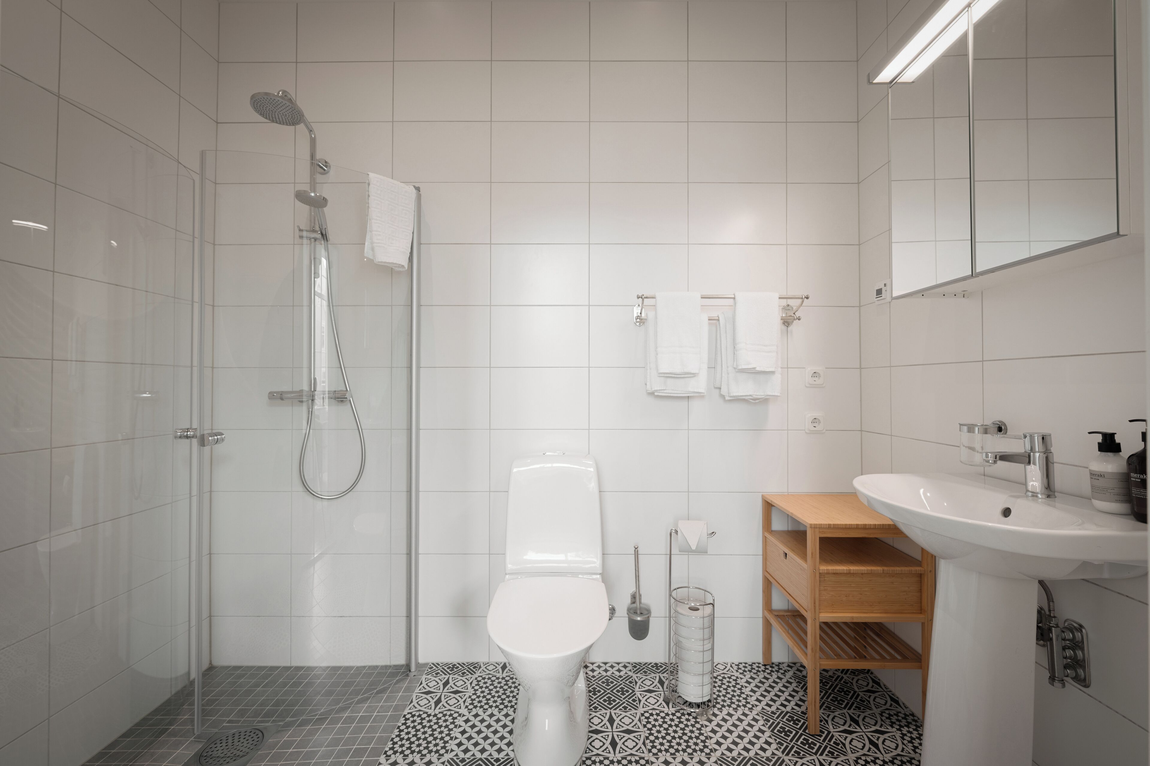Et moderne badeværelse med brusebad, toilet, vask og spejl.