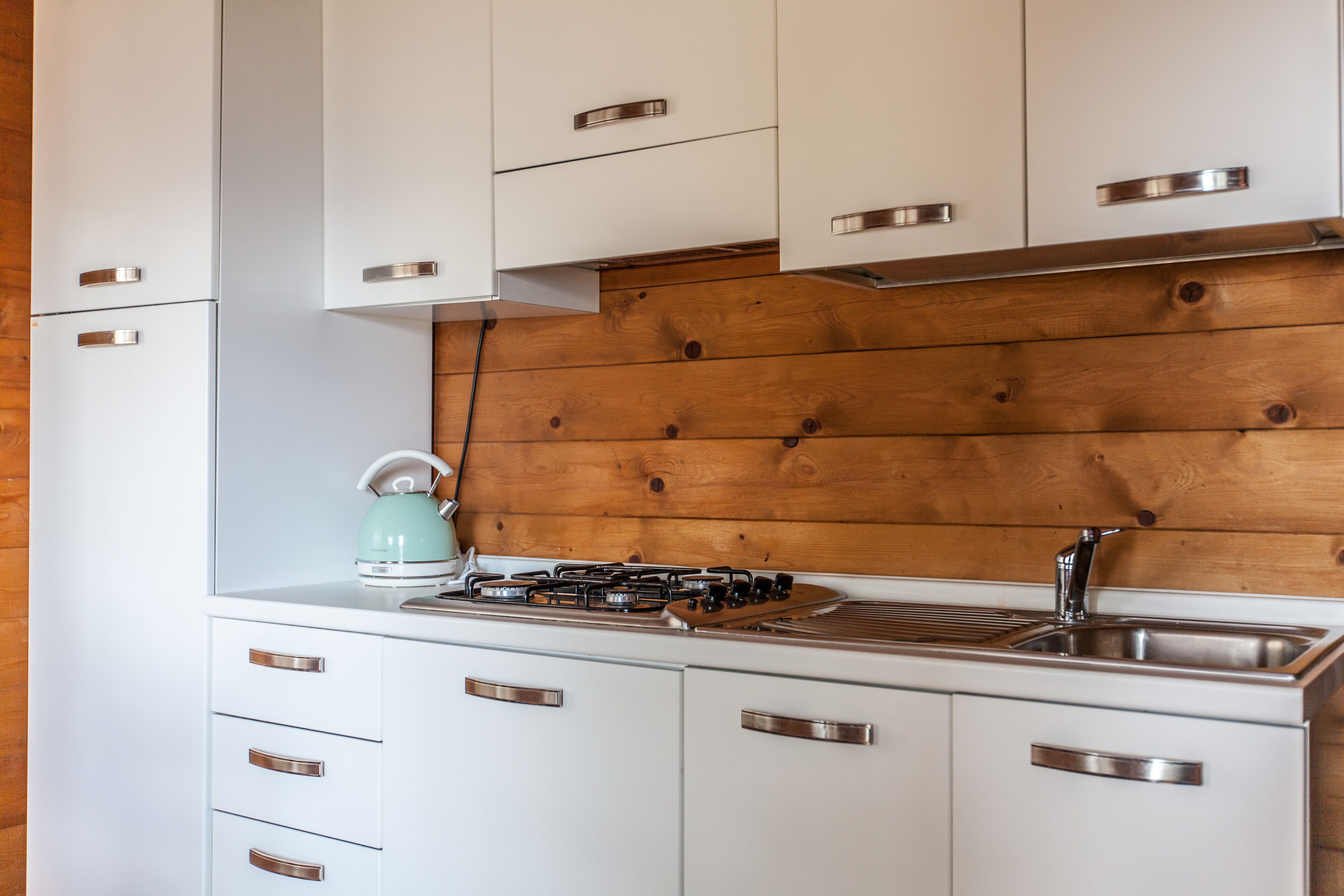 Una cocina moderna con armarios blancos, tiradores de acero inoxidable, una estufa a gas y un salpicadero de madera.
