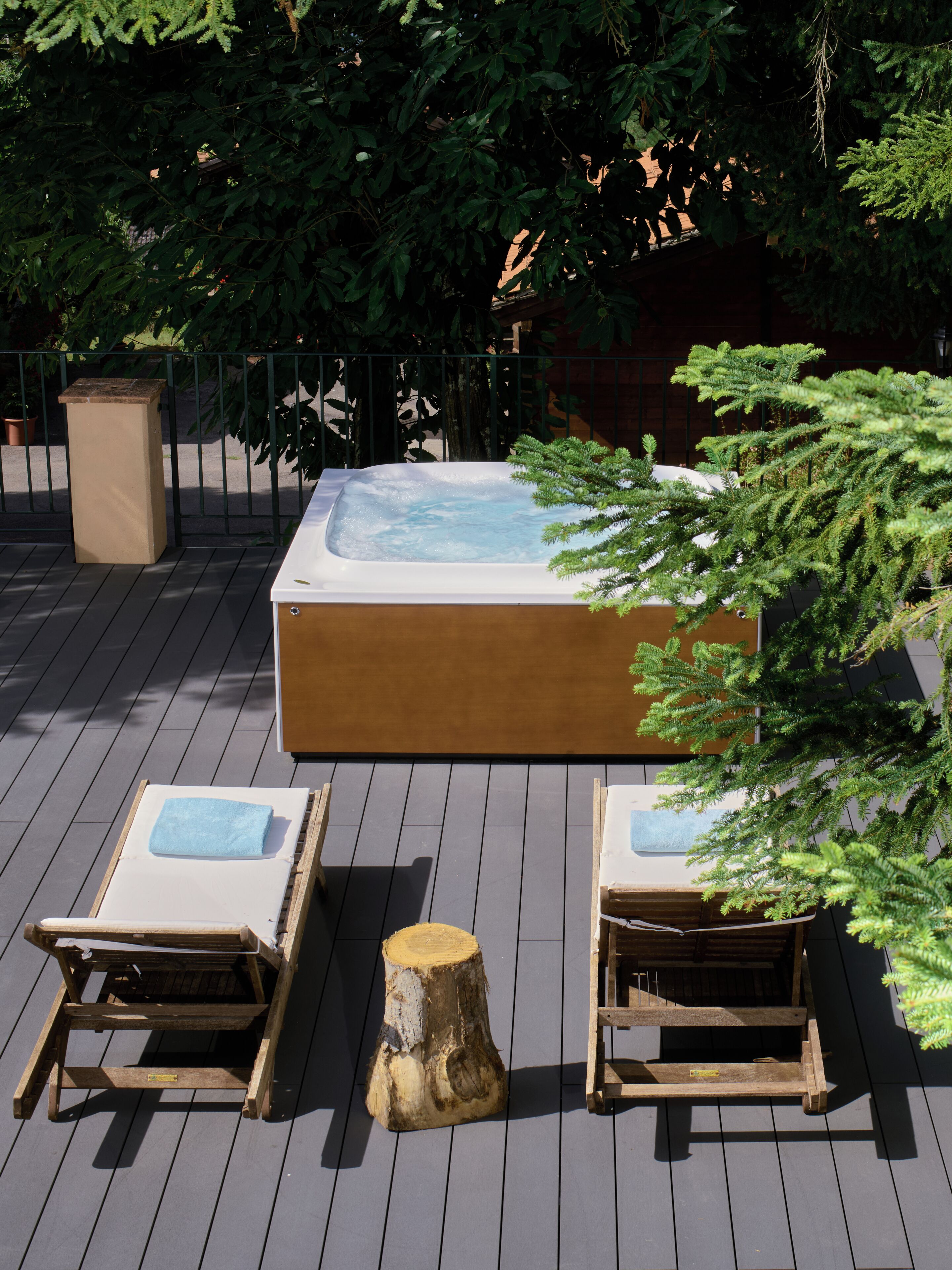 A hot tub with two wooden lounge chairs, surrounded by greenery and a wooden deck.