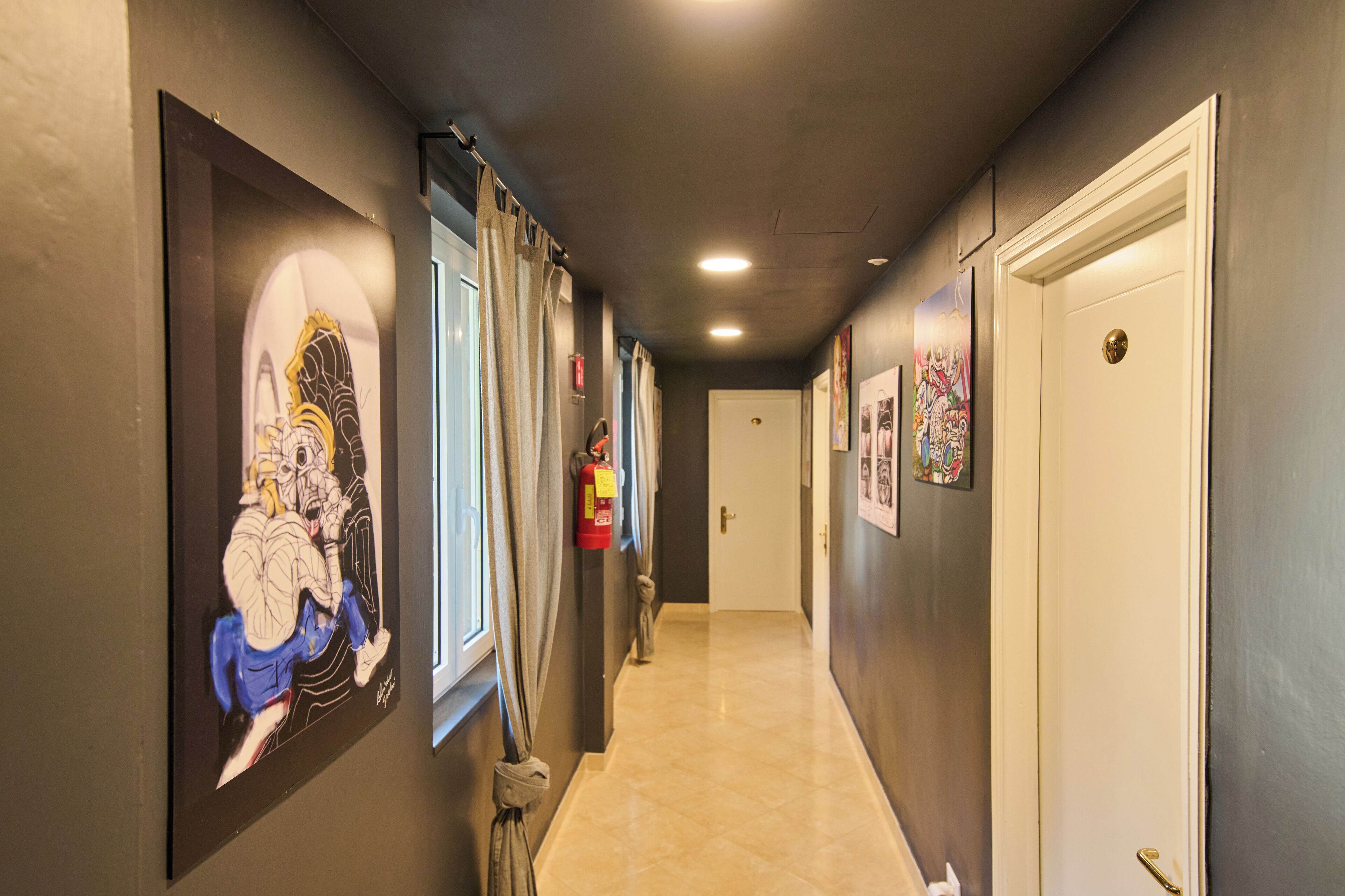 Un couloir orné d’œuvres d’art, avec un extincteur sur un mur et une porte au bout.