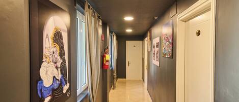 Un couloir orné d’œuvres d’art, avec un extincteur sur un mur et une porte au bout.