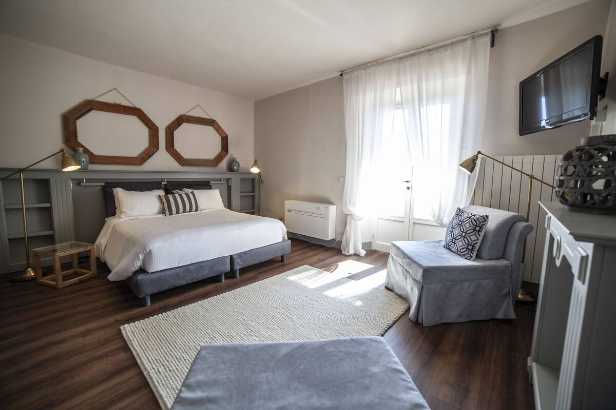 A bedroom with a bed, bedside tables, a desk, a chair, a TV, and a window with curtains.
