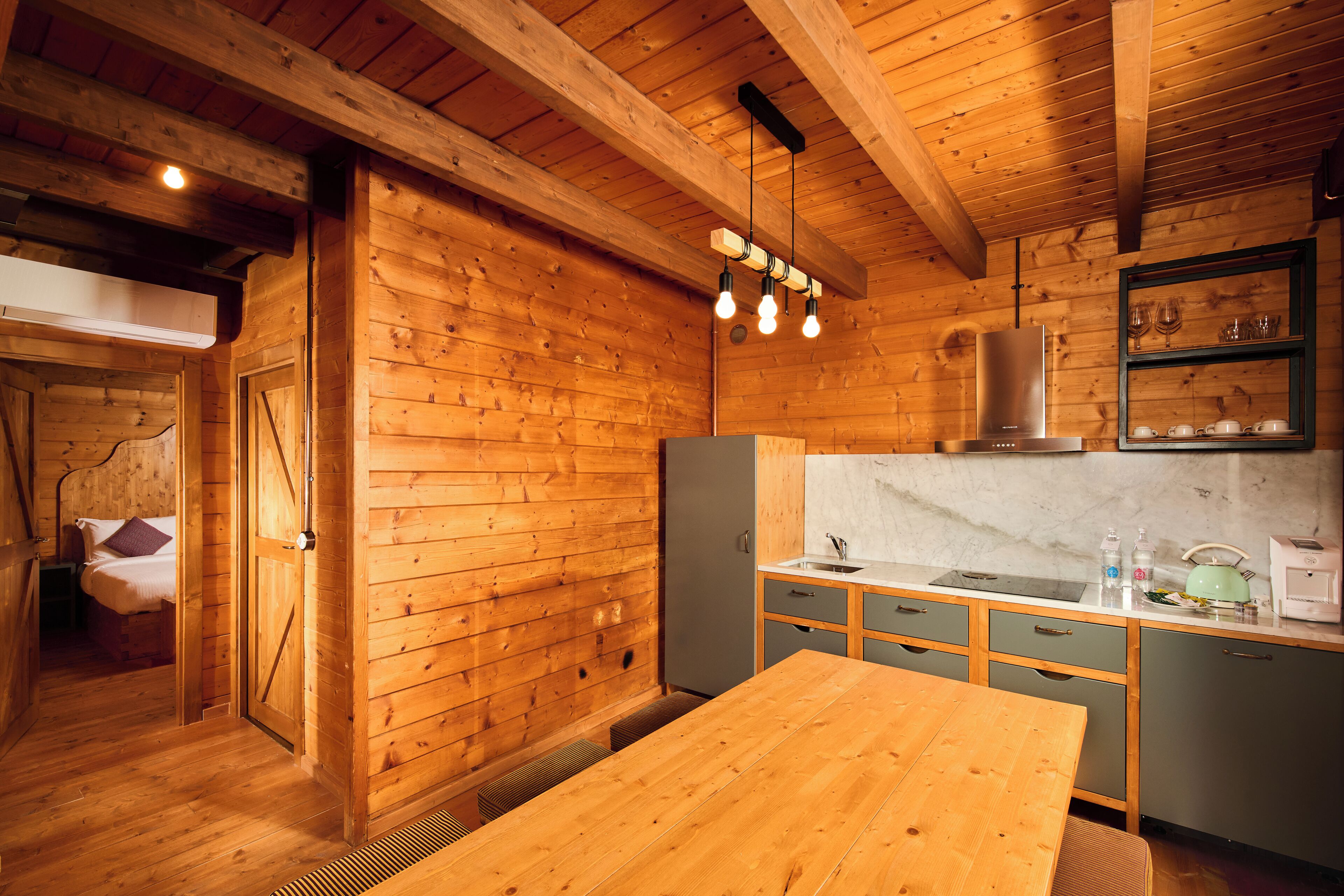 L’intérieur d’un chalet en bois comprend un coin cuisine, une table à manger et un lit donnant sur l’extérieur.
