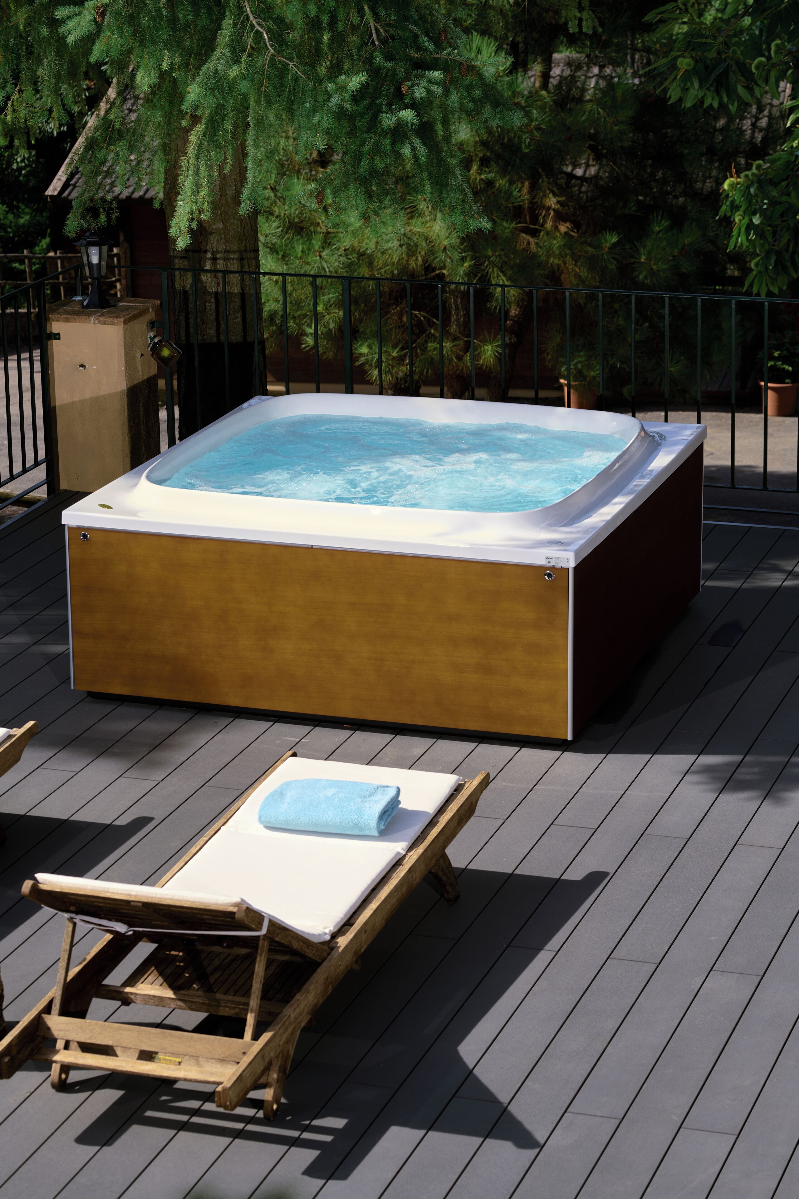 A hot tub on a wooden deck with a lounge chair and a small table.