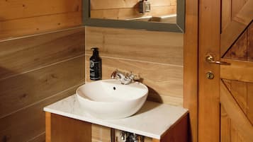 A wooden cabin bathroom with a white sink, a mirror, and a towel on a shelf.