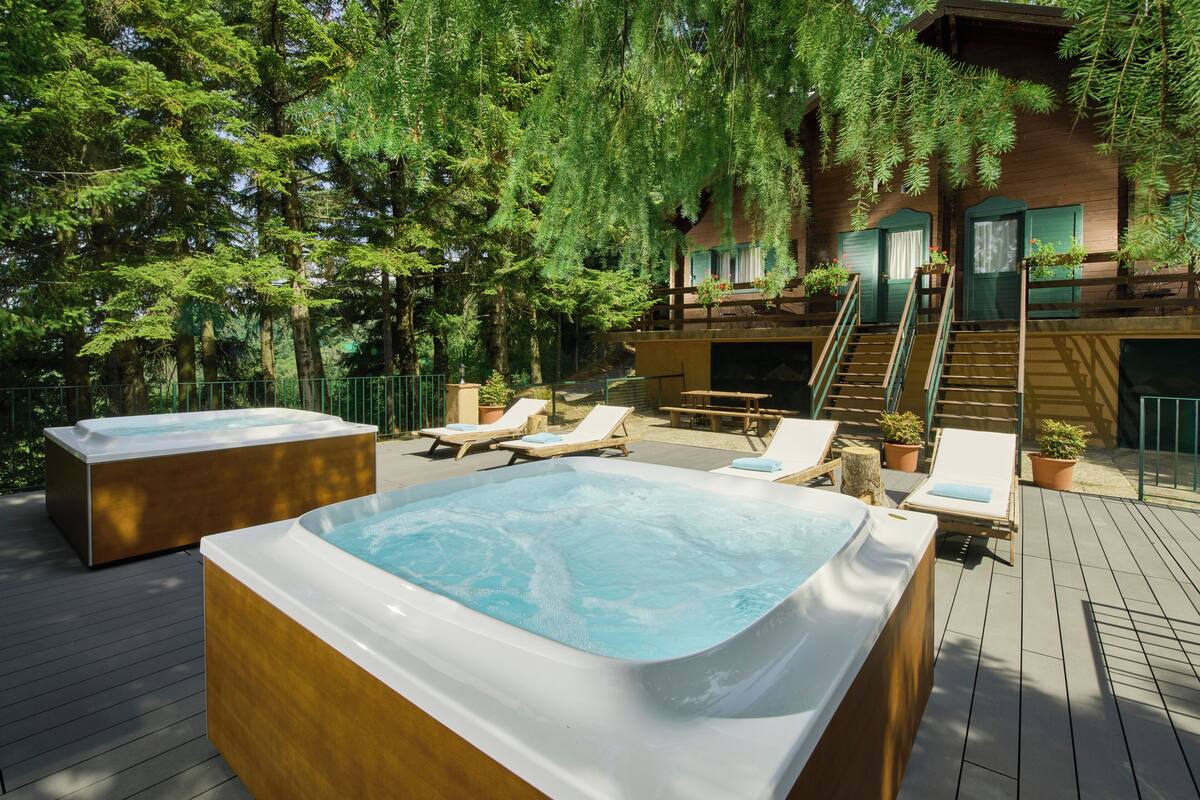 A wooden deck with two hot tubs, lounge chairs, and a staircase leading to a building.