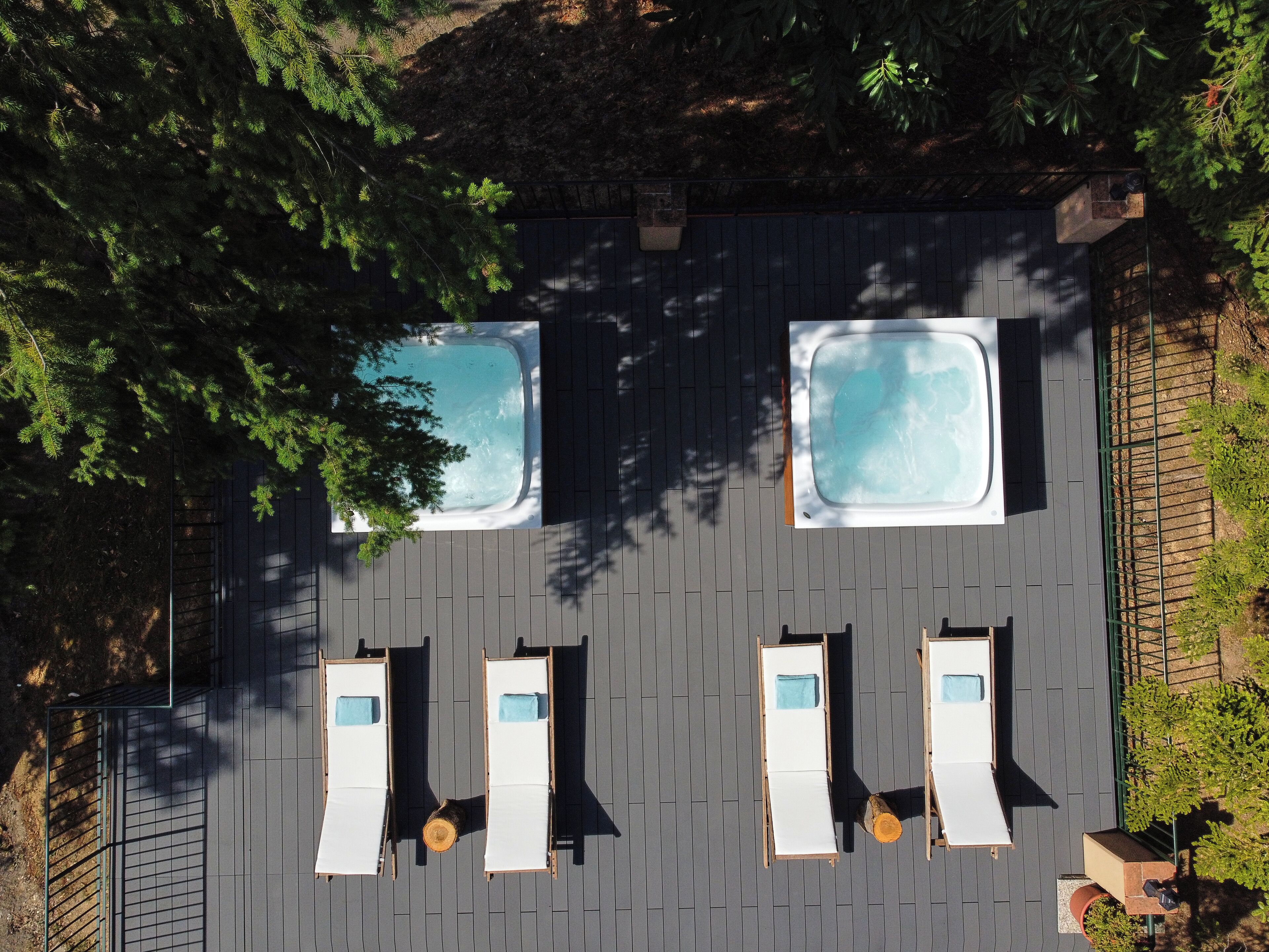 An aerial view of a rooftop with two hot tubs and four lounge chairs arranged in pairs.