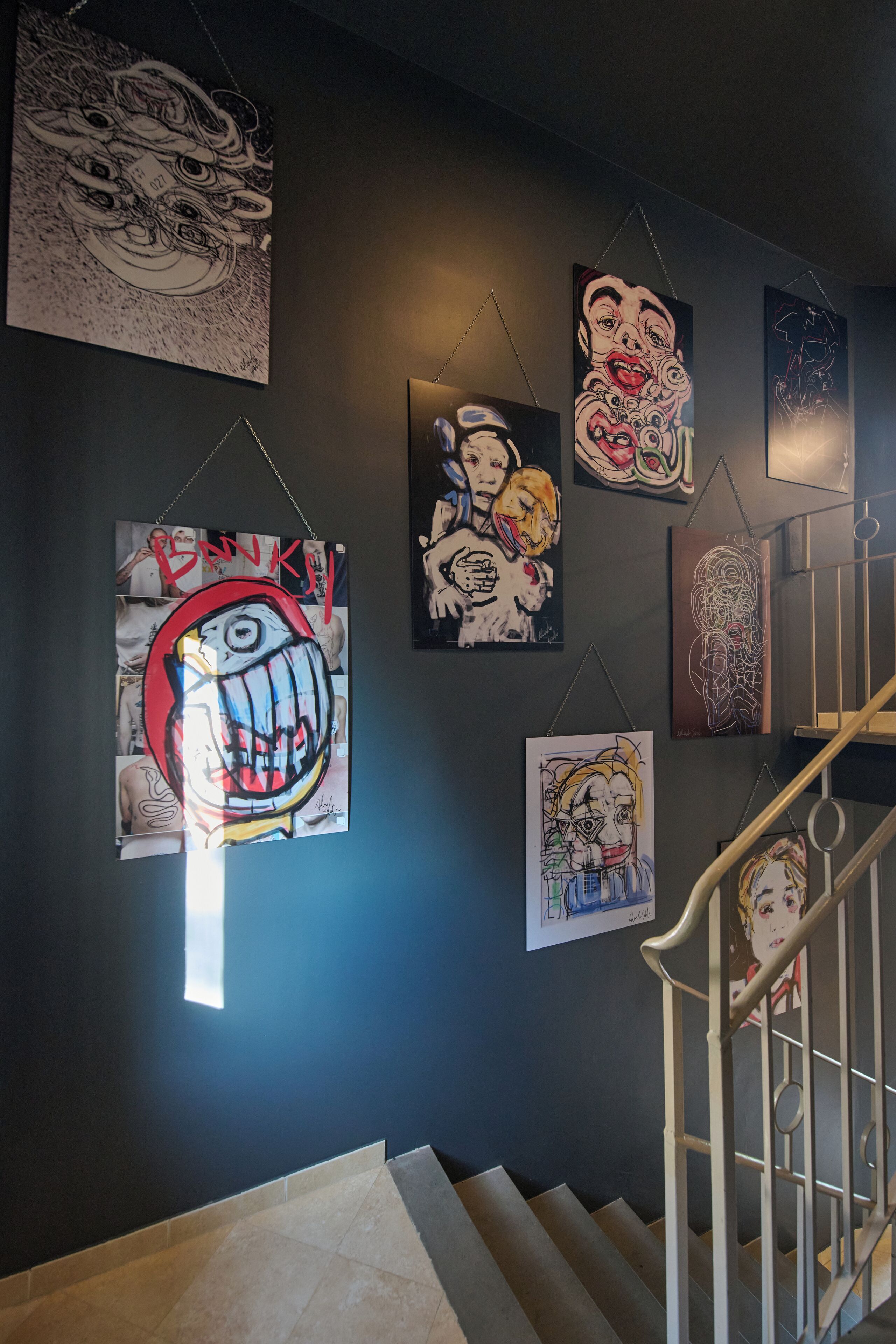 Una escalera con barandilla y una pared decorada con varias obras de arte.
