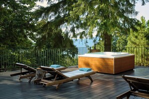 A wooden deck with lounge chairs and a hot tub, surrounded by trees and overlooking a body of water. - Il Ciocco Hotels (Barga)