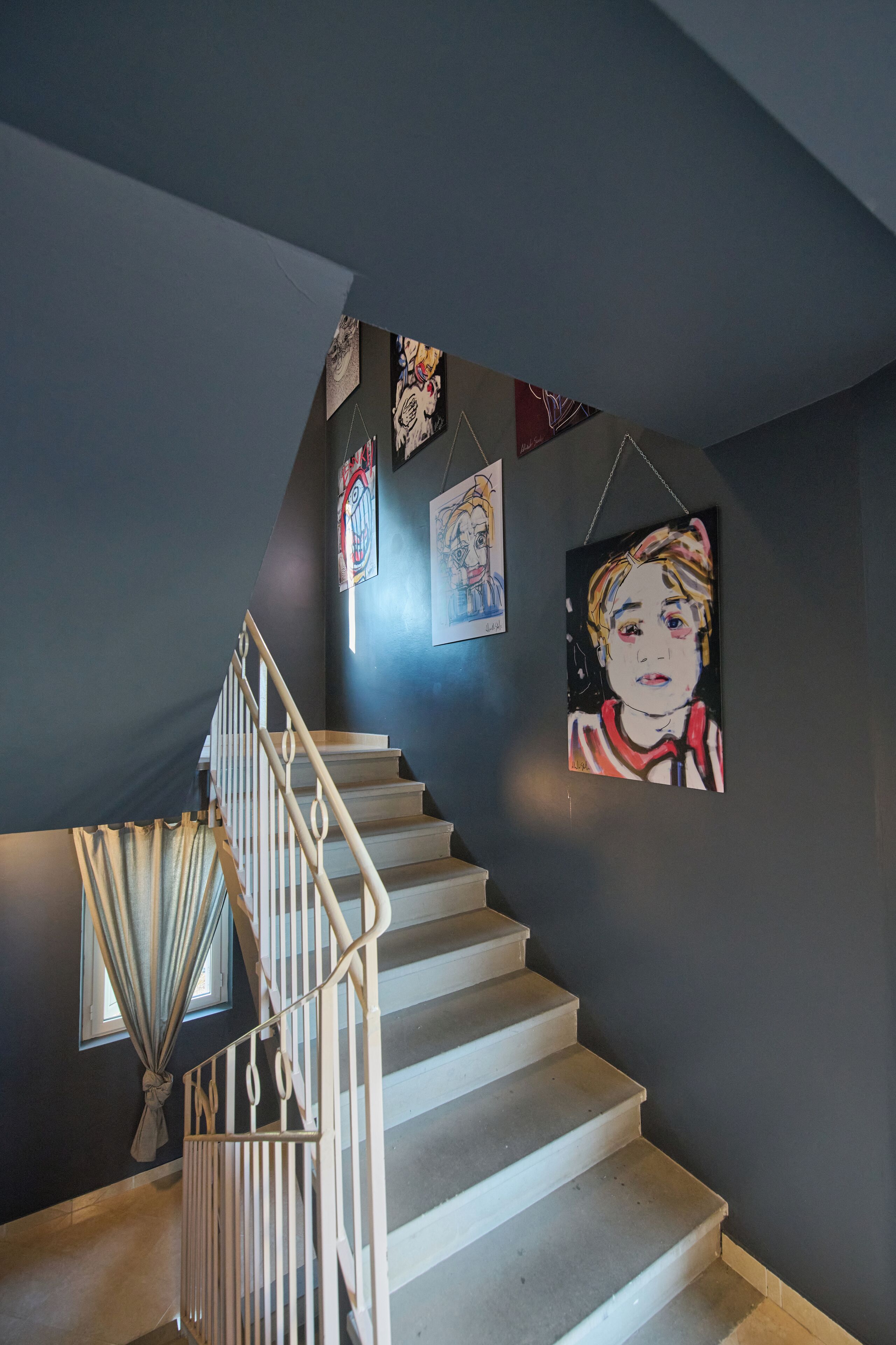 A staircase with a handrail, a window with curtains, and several artworks on the wall.