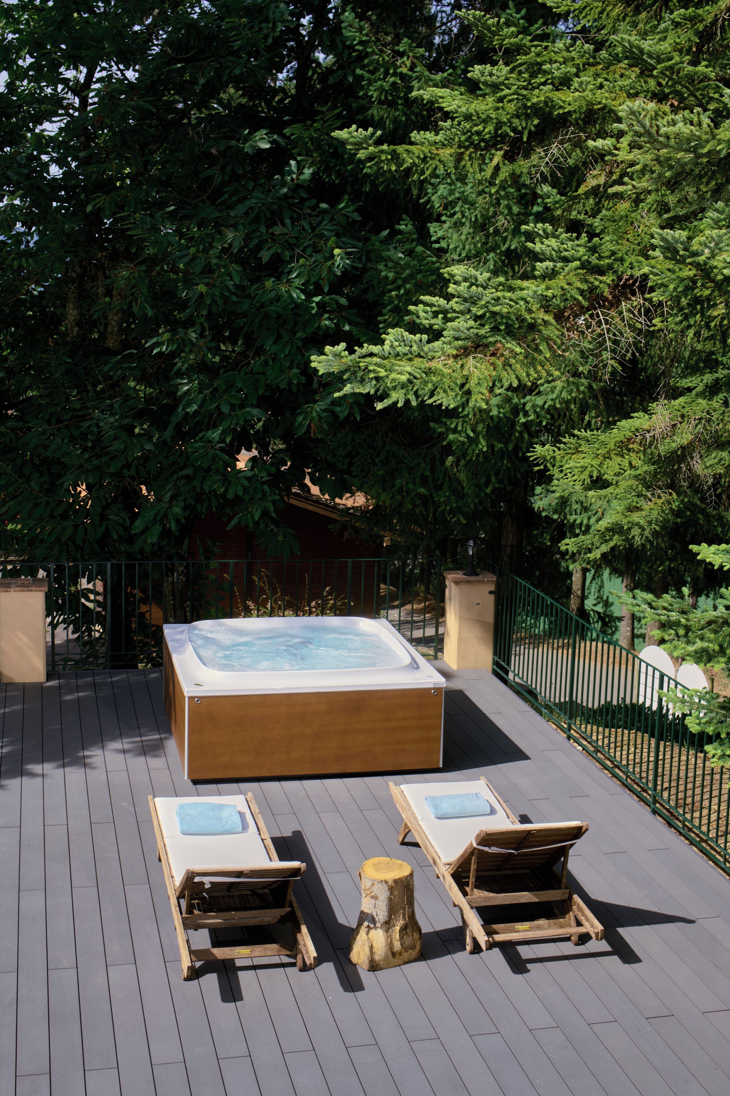 Un jacuzzi en una terraza de madera con dos sillones reclinables y un tocón de árbol.