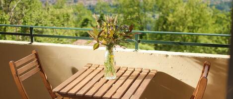 A wooden table and chairs on a balcony with a view of a green landscape.
