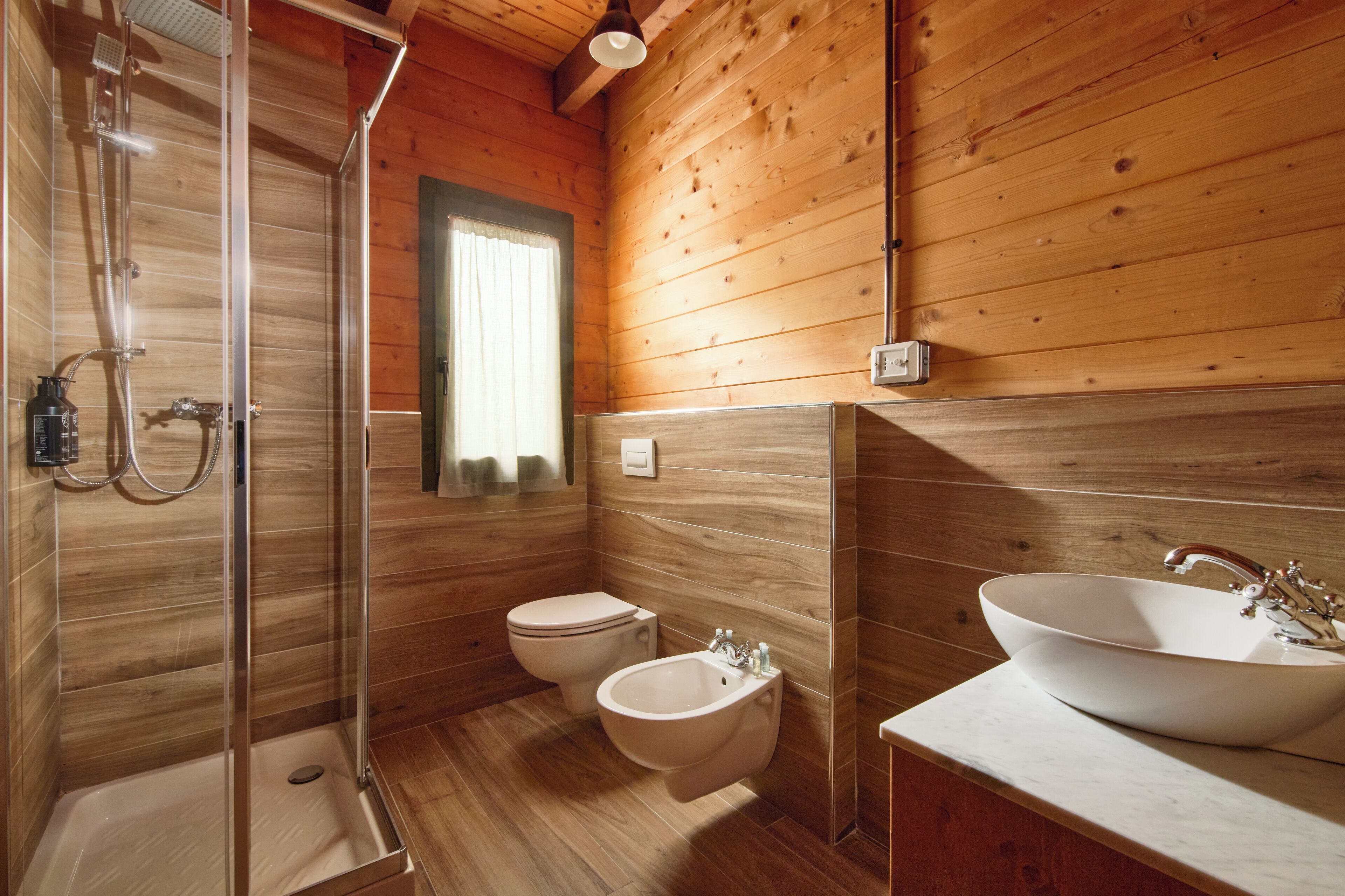 A wooden cabin bathroom with a glass shower enclosure, a toilet, a bidet, and a large vessel sink.