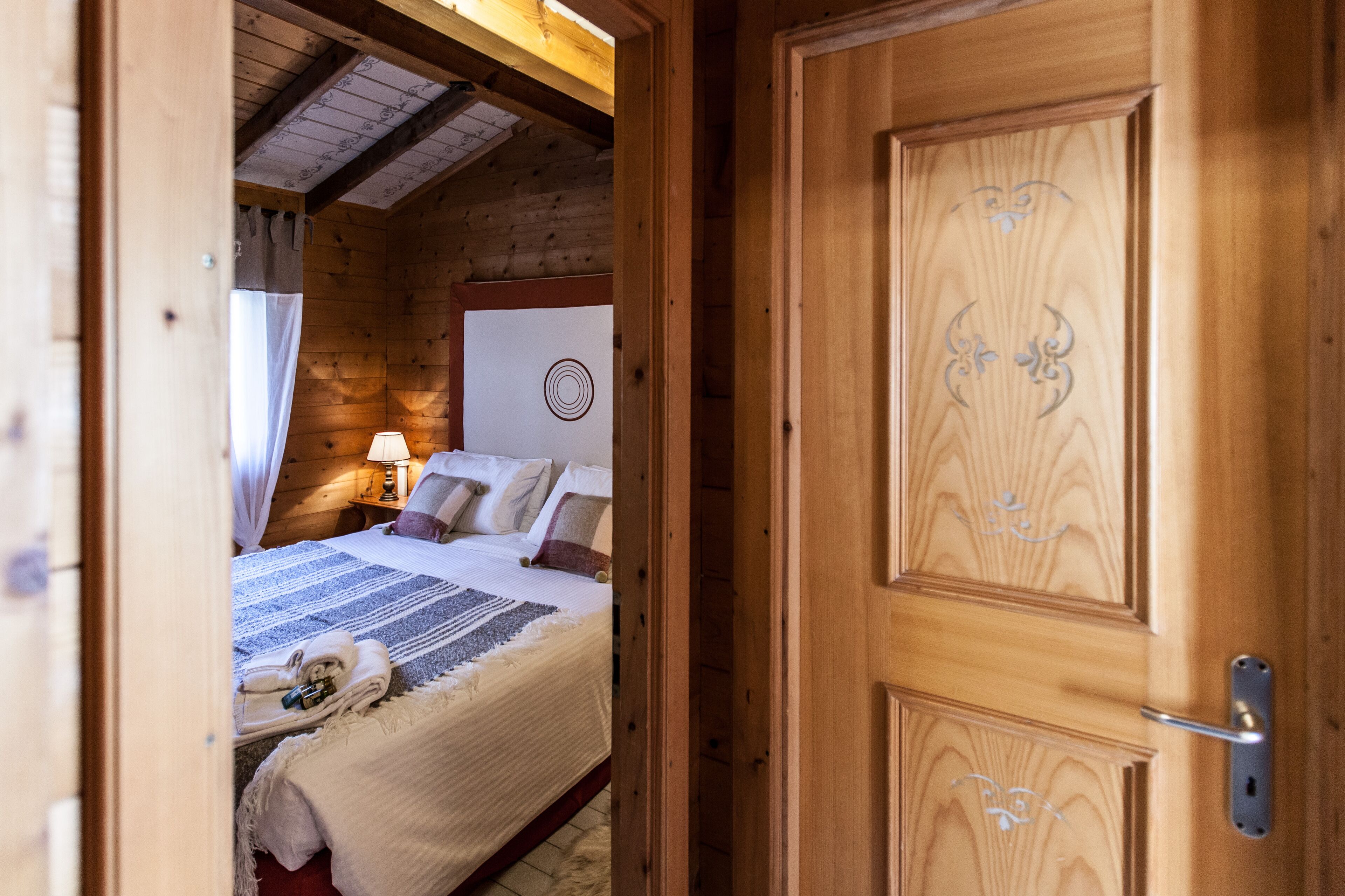Een houten slaapkamer met een bed, kussens, een nachtkastje, een lamp en een handdoek op de vloer.
