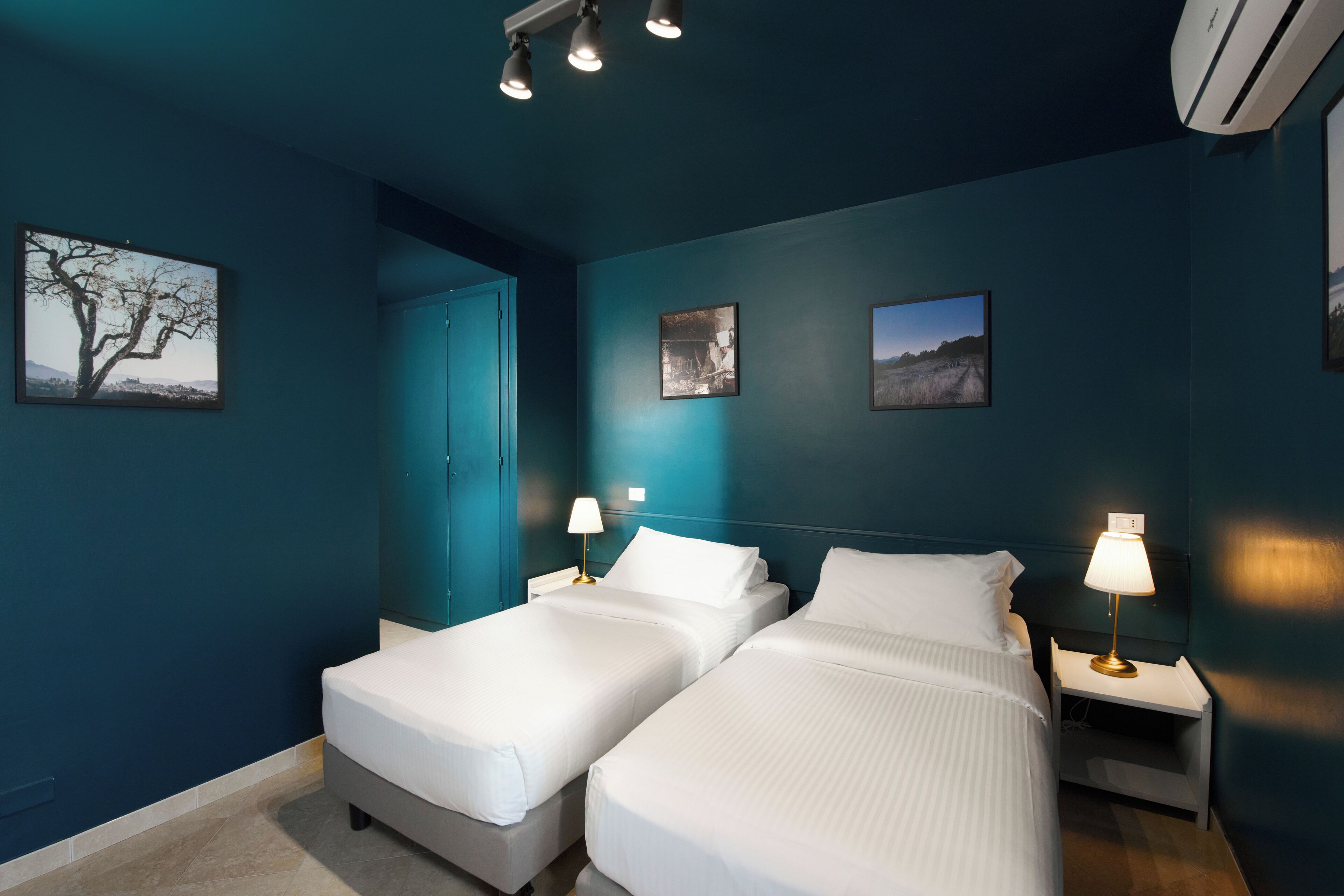 Habitación de hotel con dos camas, una mesita de noche con lámpara y aire acondicionado instalado en la pared.