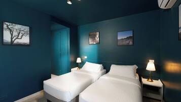 Ein Hotelzimmer mit zwei Betten, einem Nachttisch mit Lampe und einer Wand-Klimaanlage.