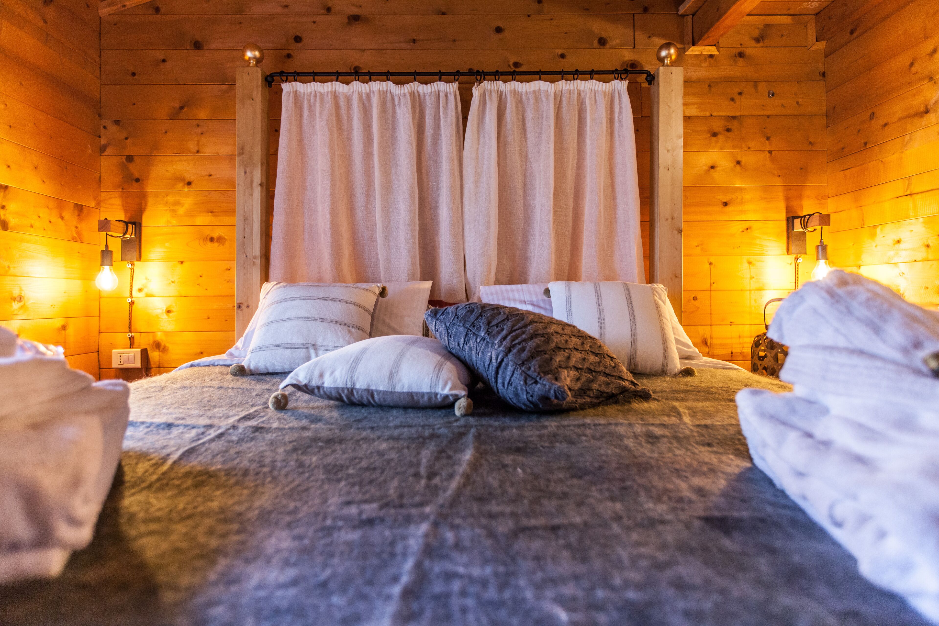 Ein Schlafzimmer einer Holzhütte mit einem Himmelbett, weißen Vorhängen und zwei Wandlampen.