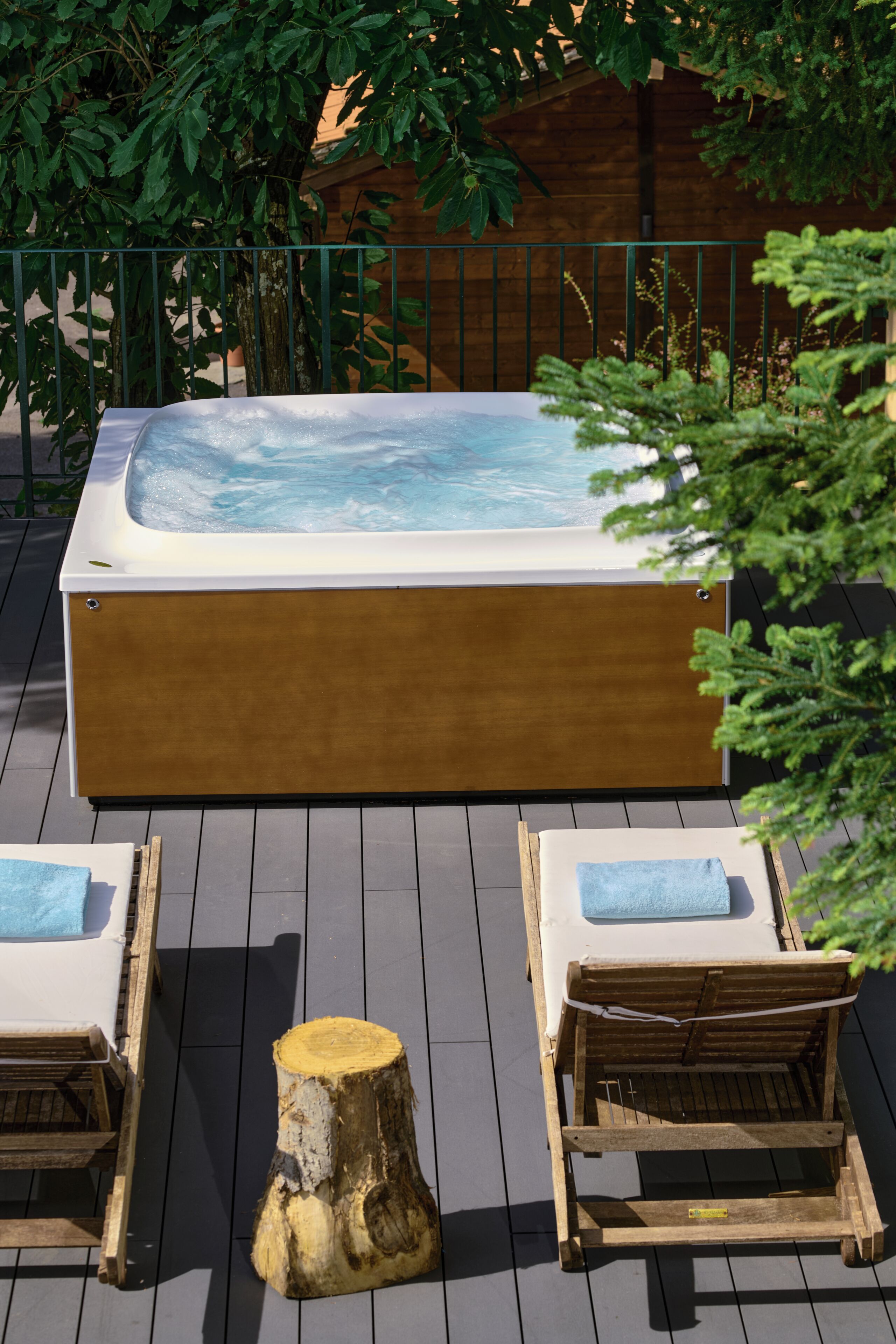 A hot tub with two lounge chairs and a wooden stump on a wooden deck.