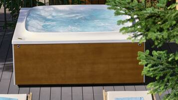 A hot tub with two lounge chairs and a wooden stump on a wooden deck.