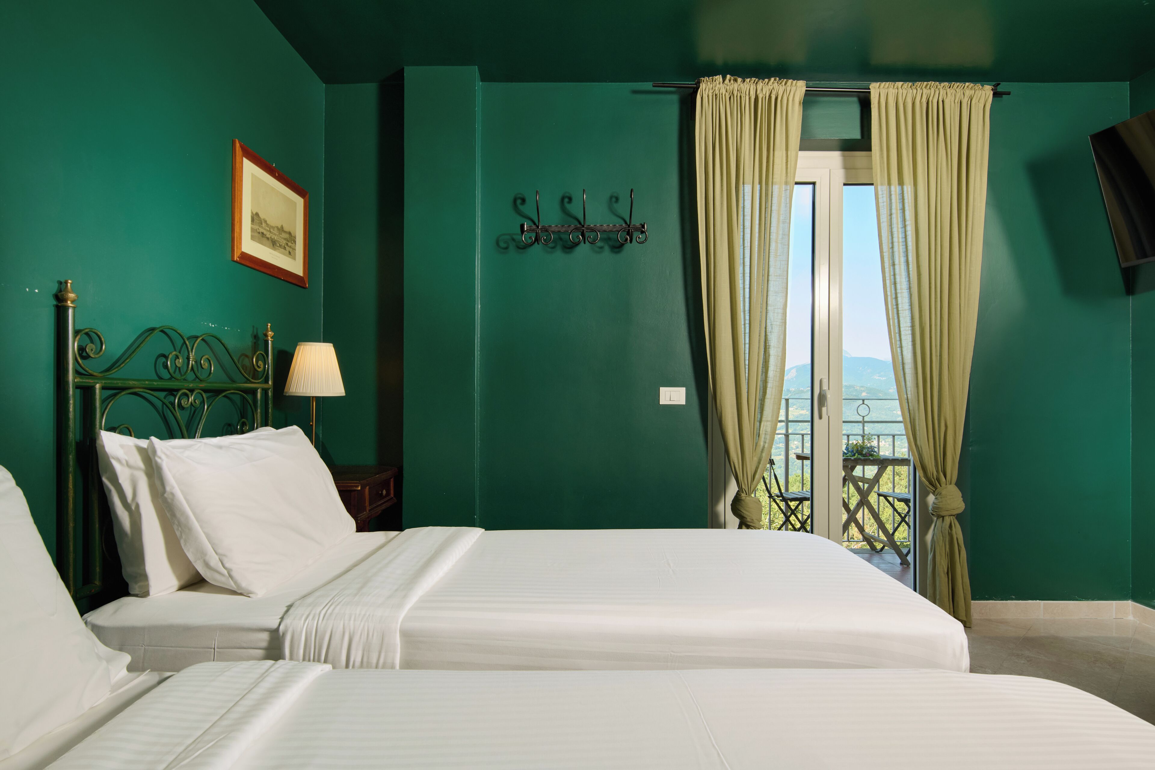 A hotel room with two beds, a window with curtains, a wall-mounted TV, and a framed picture.