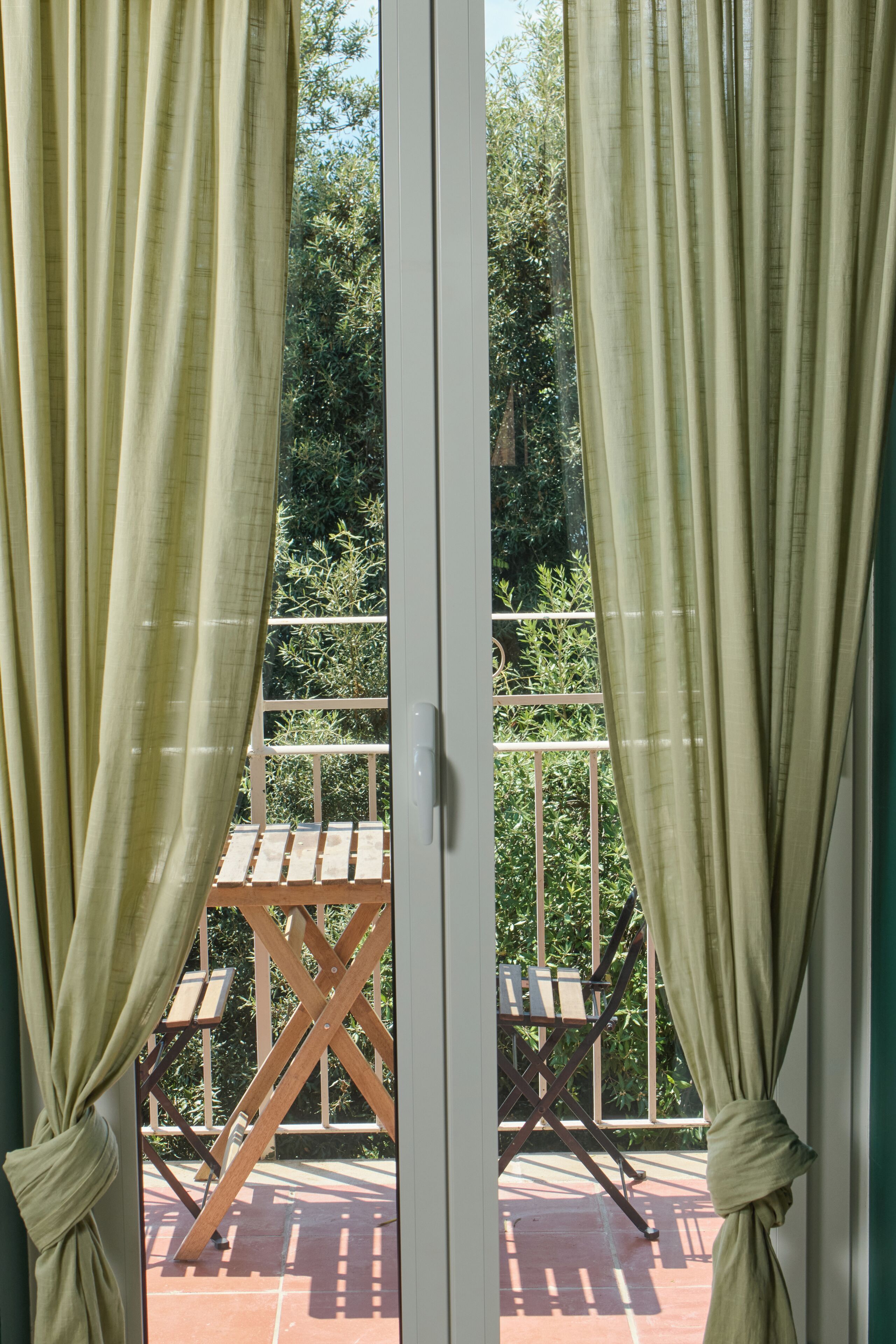 Une vue à travers une porte vitrée, derrière laquelle on aperçoit des rideaux, donnant sur une terrasse en bois avec une table et des chaises.