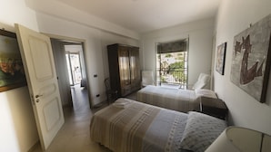 Ein Hotelzimmer mit zwei Betten, einem Kleiderschrank, einem Sessel, einem Schreibtisch und einem Fenster mit Blick nach außen.
