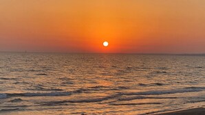 Ein Sonnenuntergang über ruhigem Meer, mit einem Schiff in der Ferne.