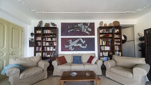 Ein Wohnzimmer mit zwei beigefarbenen Sofas, einem Holztisch und zwei Bücherregalen voller Bücher und Dekoartikeln.