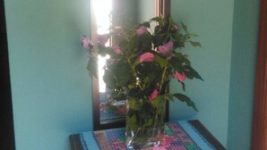 A wooden bedside table with a vase of pink flowers and a mirror above it.