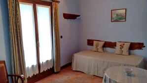 A room with a bed, a chair, a small table with a bowl, and a painting on the wall.