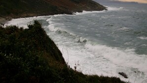 A coastal landscape with rugged terrain and a turbulent sea.