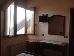 A bedroom with a bed, a desk, a mirror, and a TV on the wall.