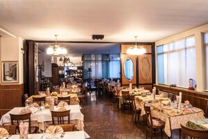 Un restaurante con varias mesas, sillas de madera y una zona de bar al fondo.