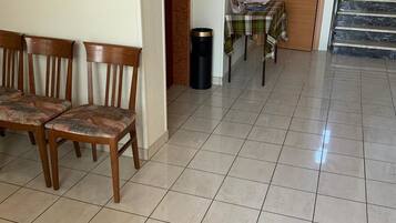 A dining area with wooden chairs and a table, a trash bin, and a calendar on the wall.