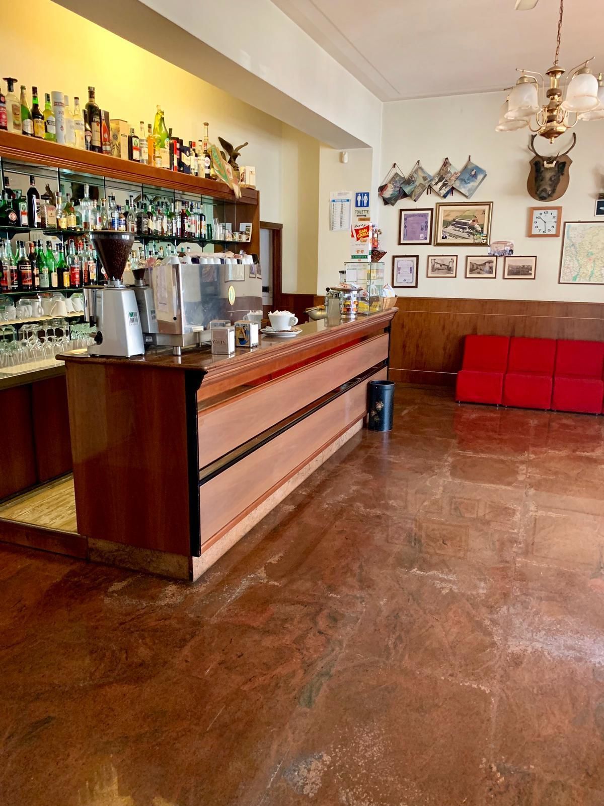 Un espace bar avec un comptoir en bois, des étagères remplies de bouteilles d’alcool, un appareil à café et un coin salon rouge.