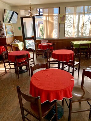 A dining area with round tables covered in red tablecloths, wooden chairs, and a view of the street through large windows.