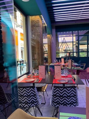 Un espace de restauration intérieur avec des tables disposées pour deux personnes, chacune étant agrémentée d’un présentoir à menus. L’espace présente un design moderne, avec des nappes et des chaises à motifs.